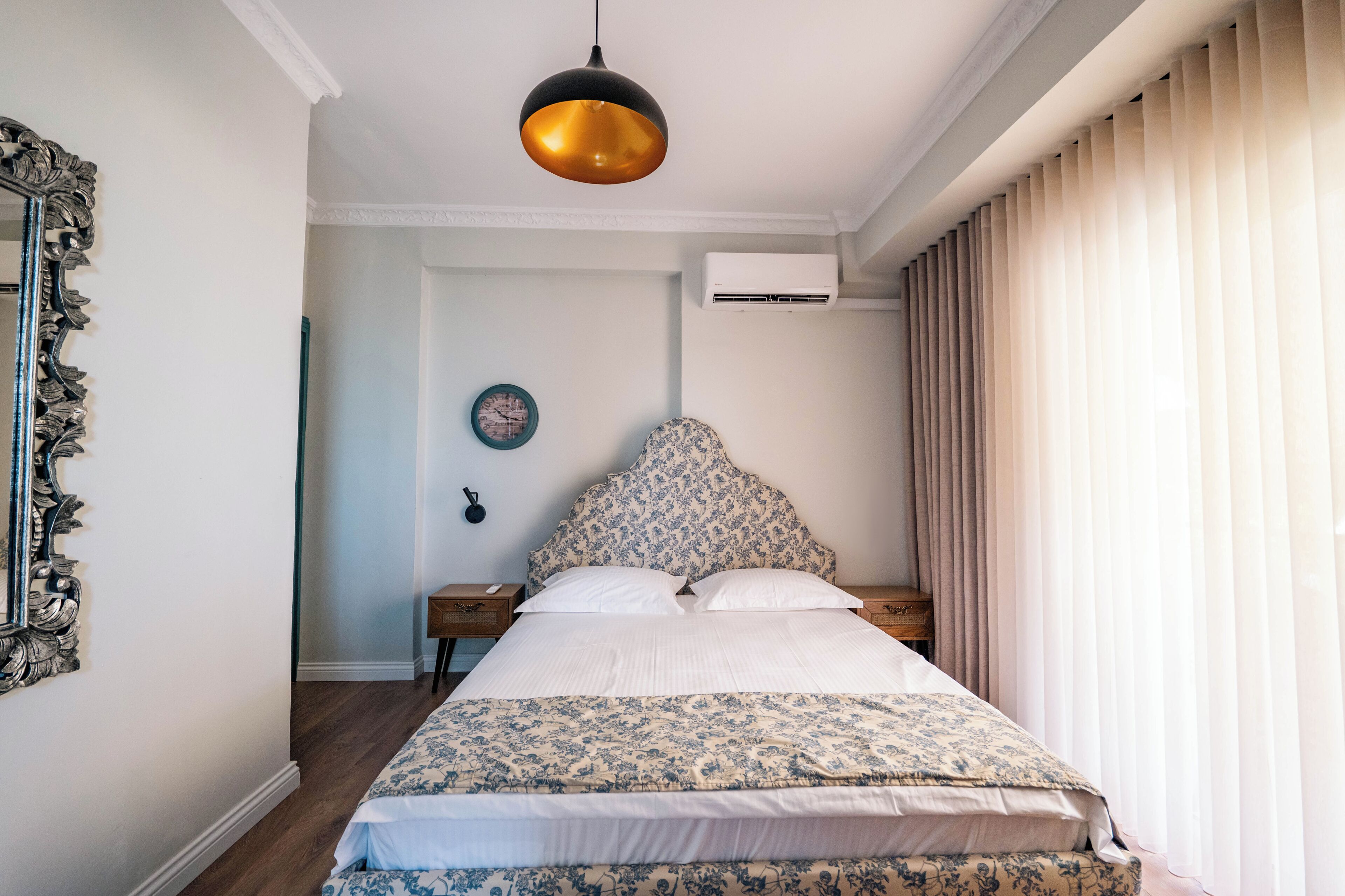 Un dormitorio con una cama grande, un espejo decorativo, un reloj de pared y un equipo de aire acondicionado.