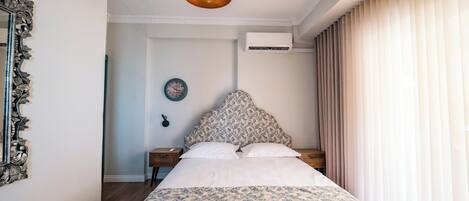 Un dormitorio con una cama grande, un espejo decorativo, un reloj de pared y un equipo de aire acondicionado.
