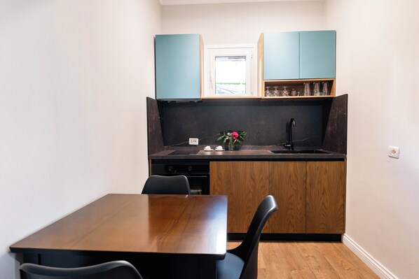 A compact kitchen with a wooden table and chairs, a black countertop, and teal cabinets. - Kristianna Apartments (Dhërmi)