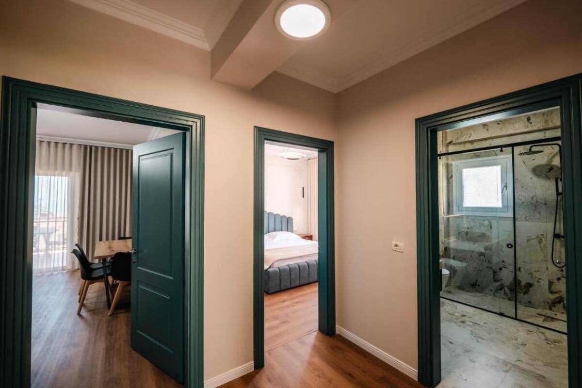A hallway with a wooden floor, a bed with a grey headboard, and a glass shower enclosure.