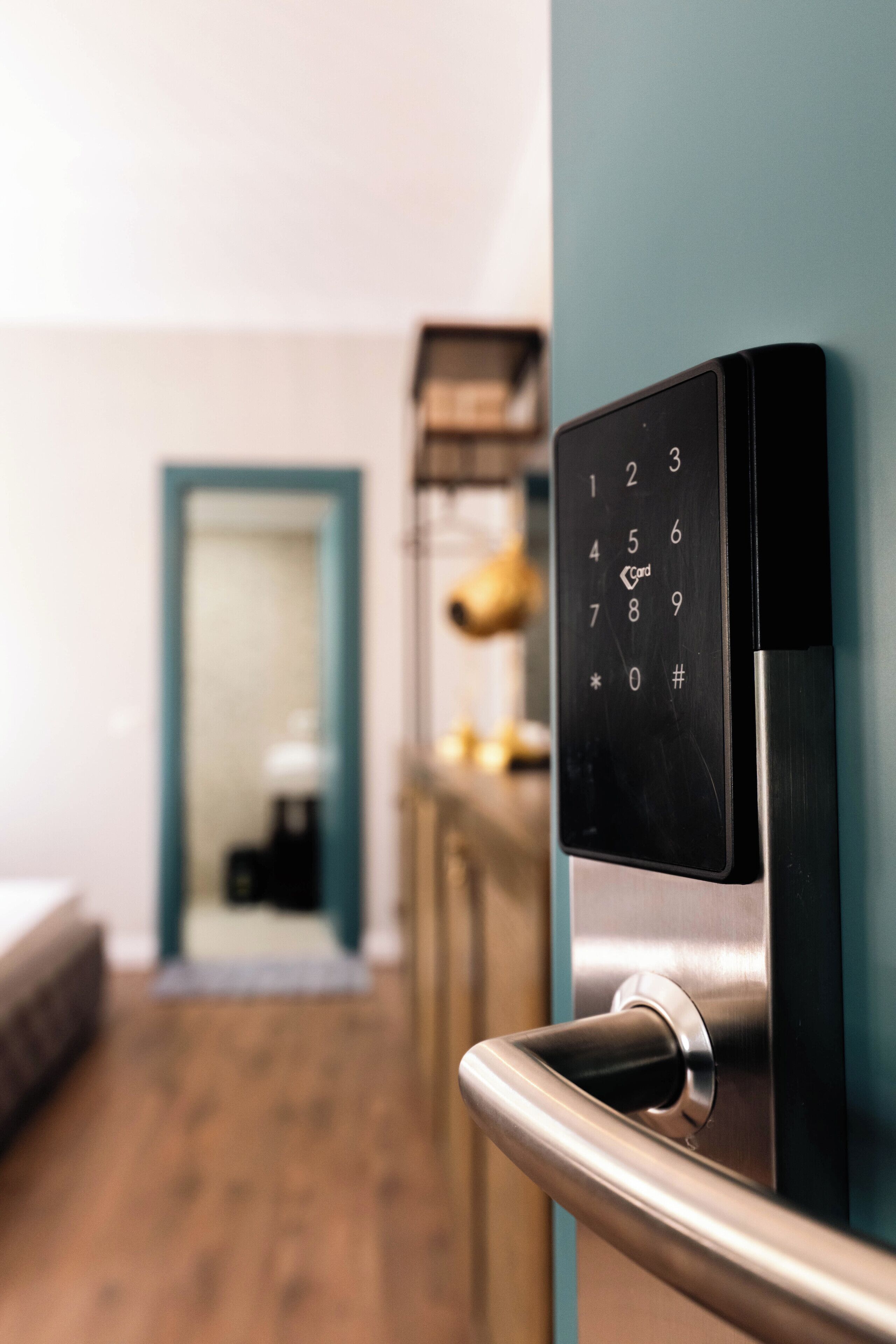 Una puerta moderna con cerradura electrónica, suelo de madera y pared color verde azulado.