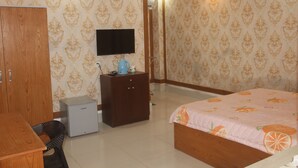 A bedroom with a bed, a desk, a small cabinet, and a television.