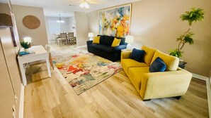 A living room with a sofa, a yellow armchair, a dining table with chairs, a ceiling fan, and a painting on the wall. - Eastgate 14A beautiful townhouse (Hammond)