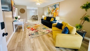 A living room with a sofa, a coffee table, a dining area with chairs, a TV, and a ceiling fan. - Eastgate 14A beautiful townhouse (Hammond)