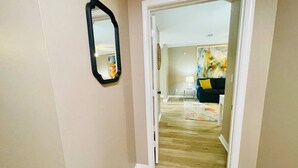 A hallway with a mirror, wooden flooring, and a door leading to a room with a painting. - Eastgate 14A beautiful townhouse (Hammond)