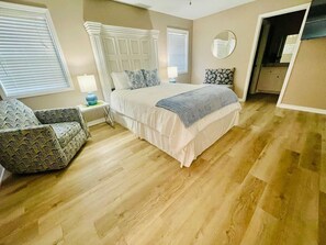 A bedroom with a bed, a chair, a bedside table, and a window.