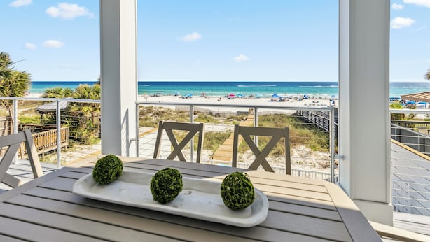 Un balcon donnant sur la plage, une table blanche agrémentée de deux objets décoratifs et une chaise en bois.
