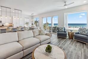 A modern living room with a large sofa, a coffee table, and a view of the ocean.