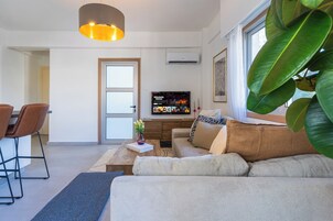 A modern living room with a sofa, coffee table, and TV. There is a dining area with chairs and a table.