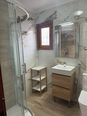 Ein Badezimmer mit Duschkabine aus Glas, Ablagefläche aus Holz, Waschbecken mit Spiegel und Toilette.