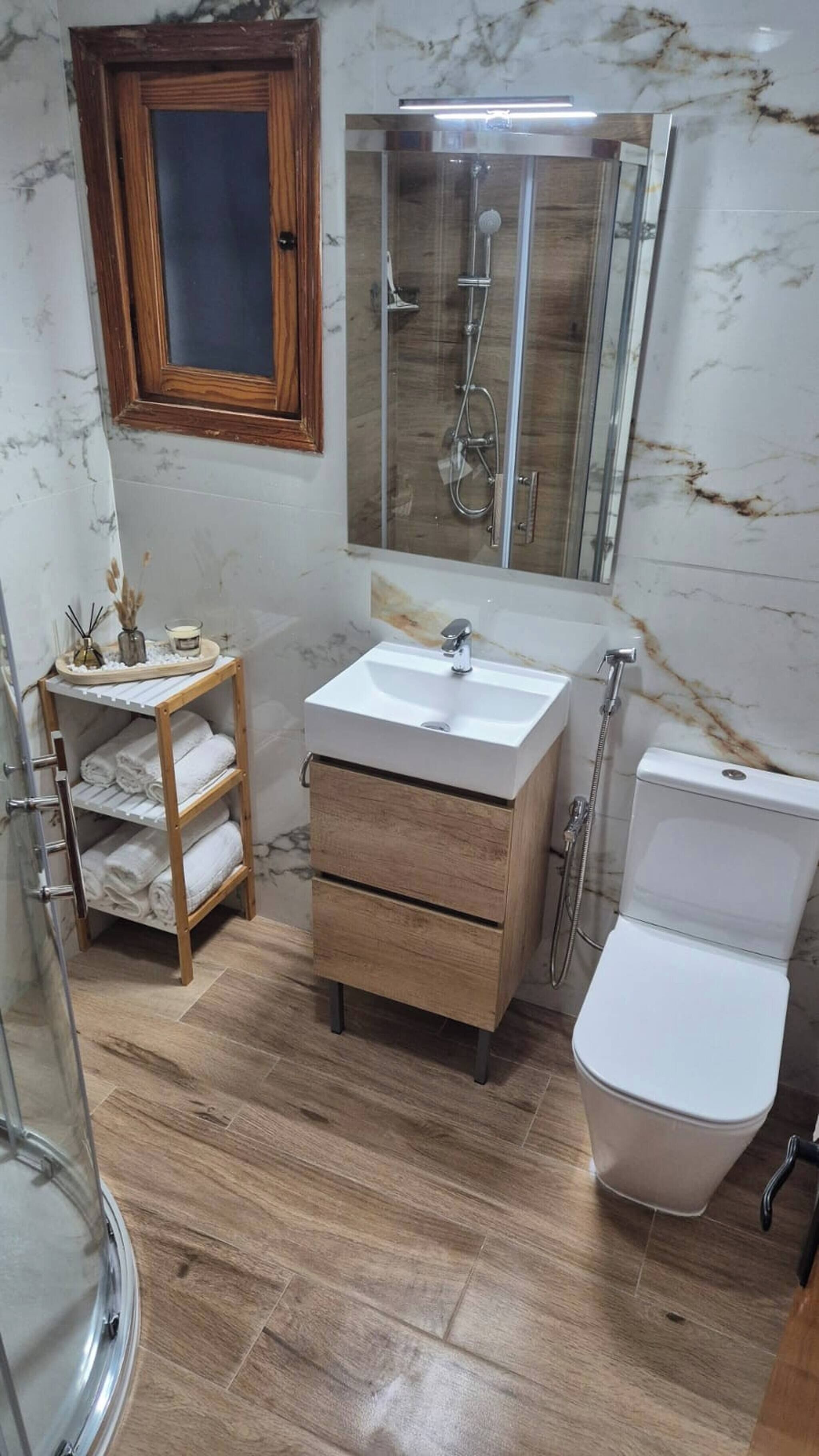 Ein Badezimmer mit einem Holzbadezimmer-Möbel, einer Duschkabine aus Glas, einer Toilette und einer Marmorwand.