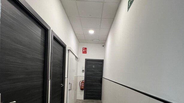 A corridor with two doors, a fire extinguisher, and a fire alarm on the wall. - Cubik Rooms (Madrid)