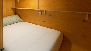 A compact, wooden interior with a single bed, a small shelf, and a ceiling light. - Cubik Rooms (Madrid)