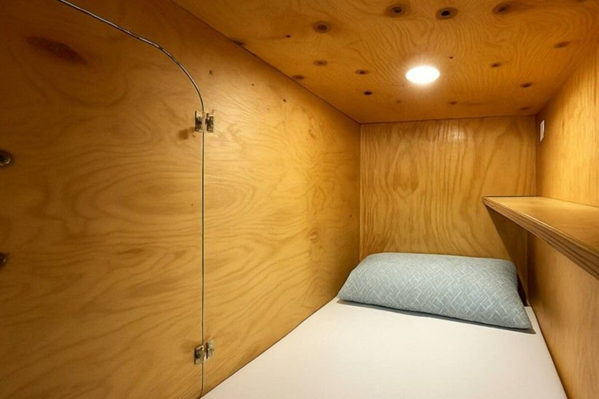 A compact room with a bed, a small bench, and a wooden ceiling with recessed lighting.