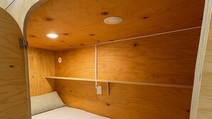 A compact, wooden interior with a bed, a shelf, and a ceiling light. - Cubik Rooms (Madrid)