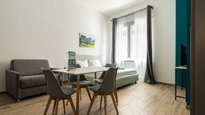 A modern room with a dining table, chairs, a sofa, a bed, and a TV. - Hotiday Torino OGR (Turin)