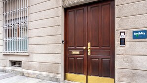 A brown double door with a brass handle and a brass plate, a keypad lock, and a 'holiday' sign on the wall. - Hotiday Torino OGR (Turin)