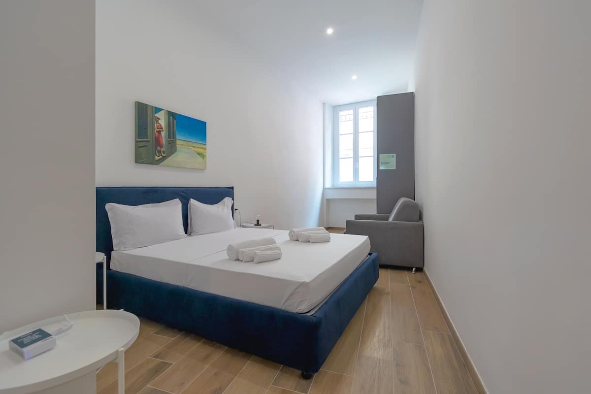 A modern hotel room with a large bed, a small desk, a chair, and a painting on the wall.