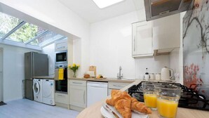 Et moderne køkken med ovenlys, komfur, vask og spiseplads med croissanter og appelsinjuice.