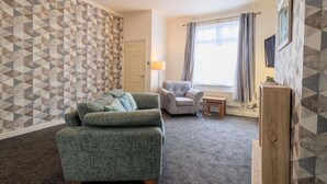 Una sala de estar con pared estampada, un sofá, un sillón, una mesita y un aparador de madera.
