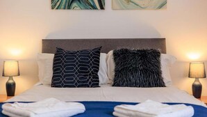 Una cama bien hecha con dos almohadas, una colcha azul y dos lámparas de noche.