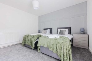 A modern bedroom with two beds, a grey headboard, a white radiator, and a grey carpet. - A comfortable home in Redcar (Redcar)