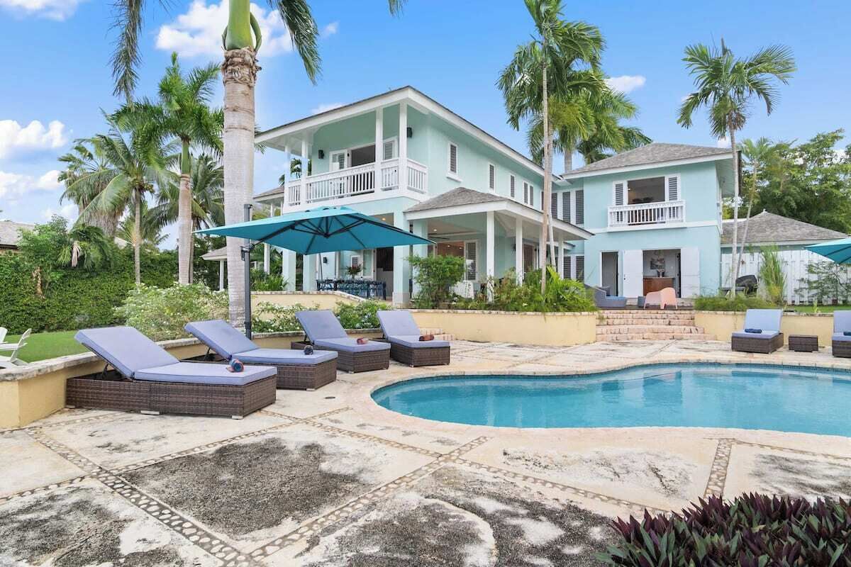 Ein zweistöckiges Haus mit Swimmingpool, umgeben von Palmen und Liegestühlen.