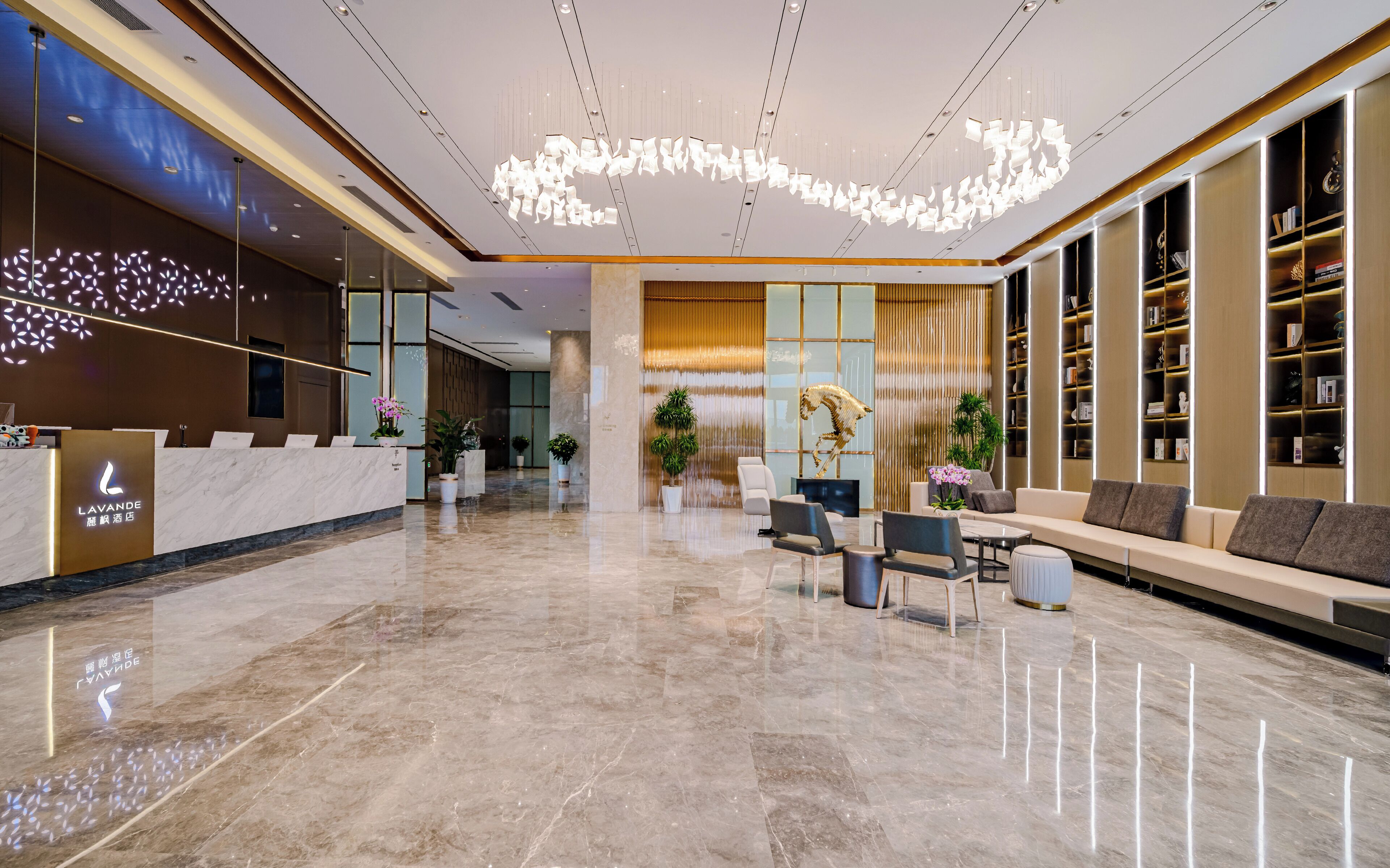 A modern hotel lobby with a reception desk, seating area, and a large bookshelf.