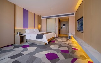Una habitación de hotel con cama, mesita de noche, lámpara y una alfombra de estampado geométrico.