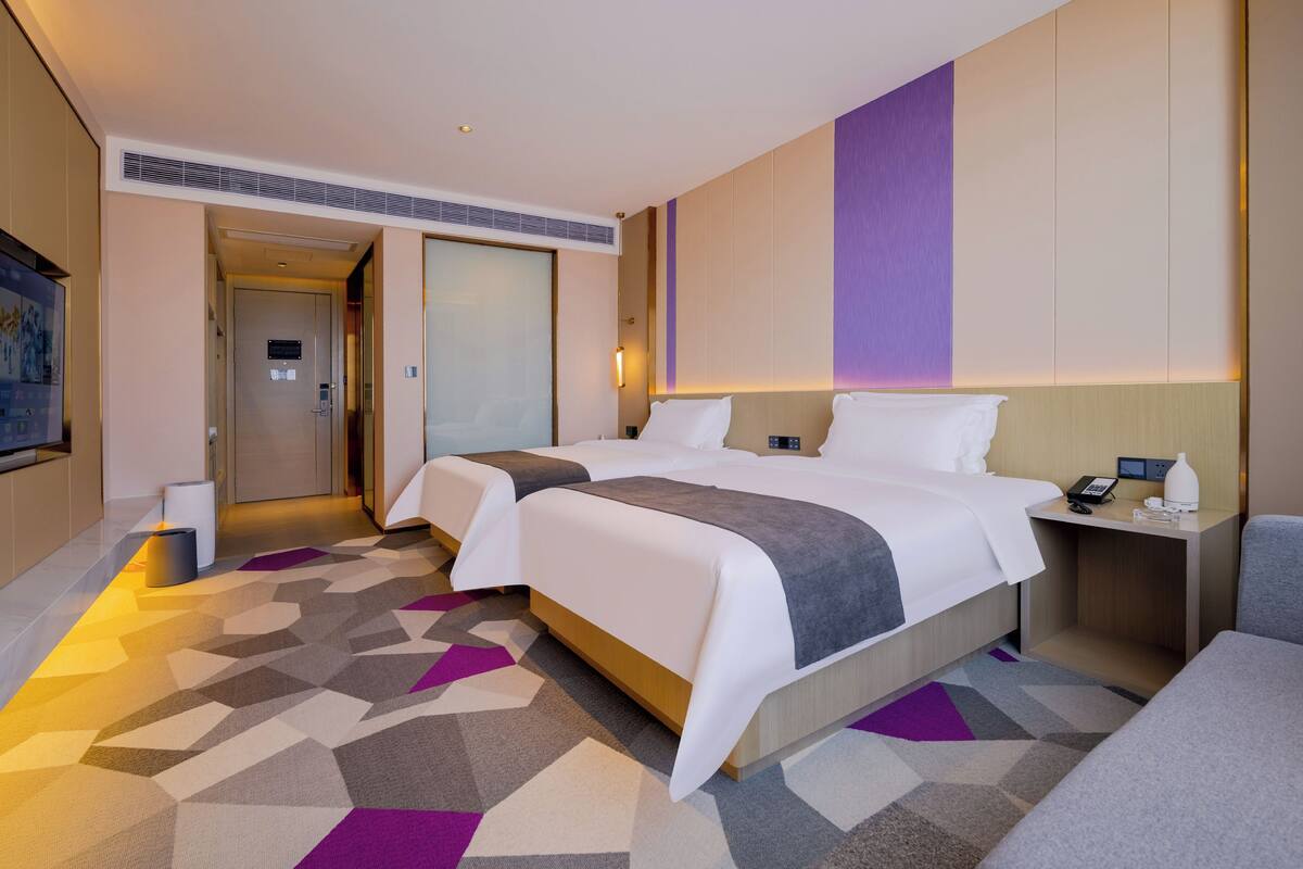 Ein Hotelzimmer mit zwei Betten, einem Schreibtisch mit Telefon und Lampe sowie einem an der Wand montierten Fernseher.