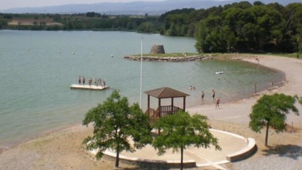 A lakeside park with a gazebo, walking paths, and a dock with people.