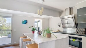 A modern kitchen with a central island, bar stools, stainless steel appliances, and a view to the outside.