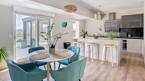 A modern kitchen with white cabinets, a black countertop, and stainless steel appliances. There is a dining area with a round table and teal chairs.