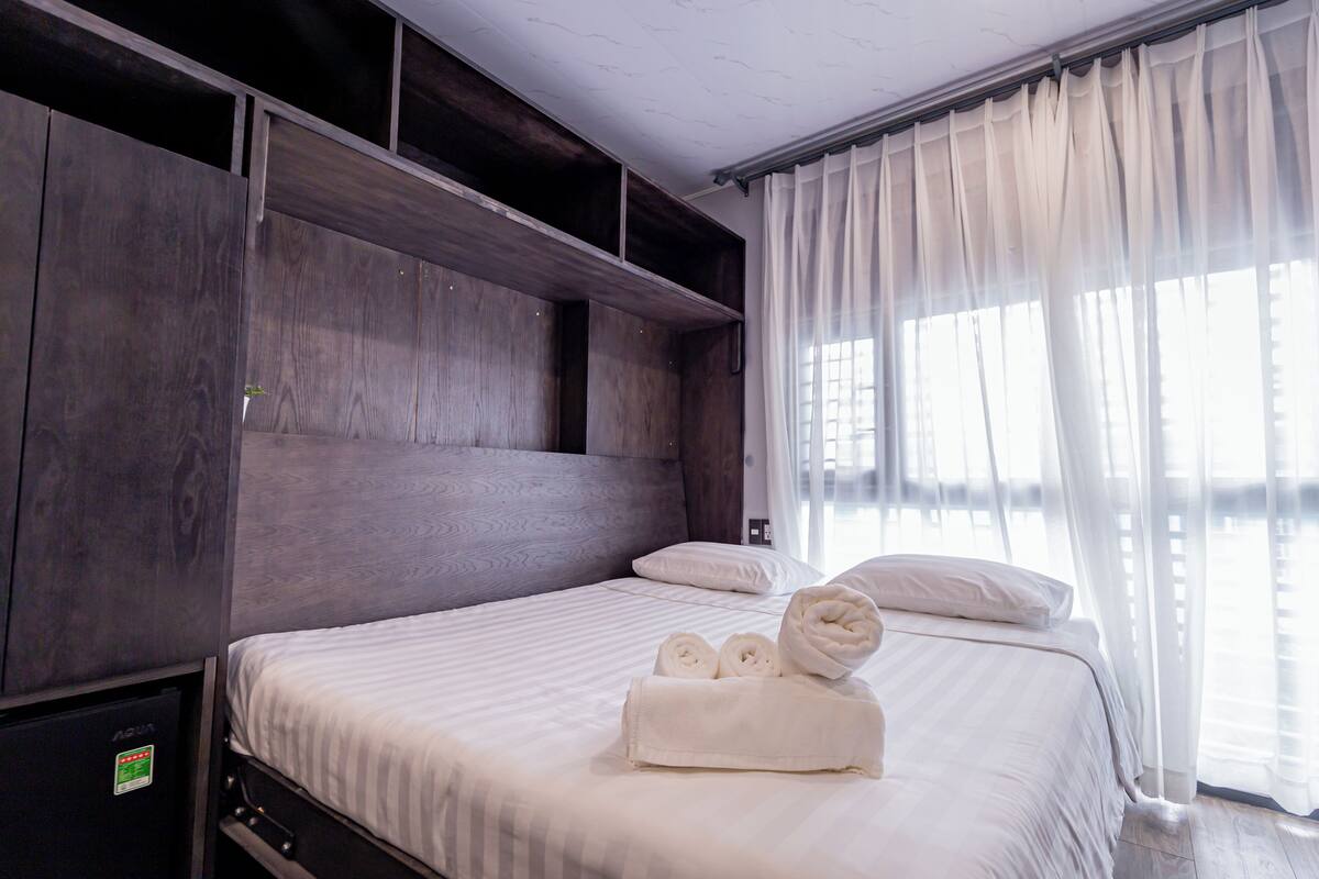 Een hotelkamer met een groot bed, een houten hoofdeinde en uitzicht door dunne gordijnen.