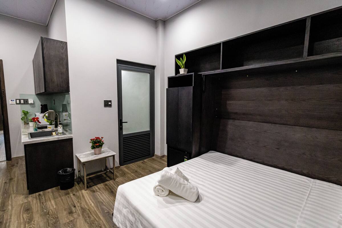 Een moderne hotelkamer met een groot bed, een klein bureau met een wasbak, een donker hoofdeinde en een potplant.