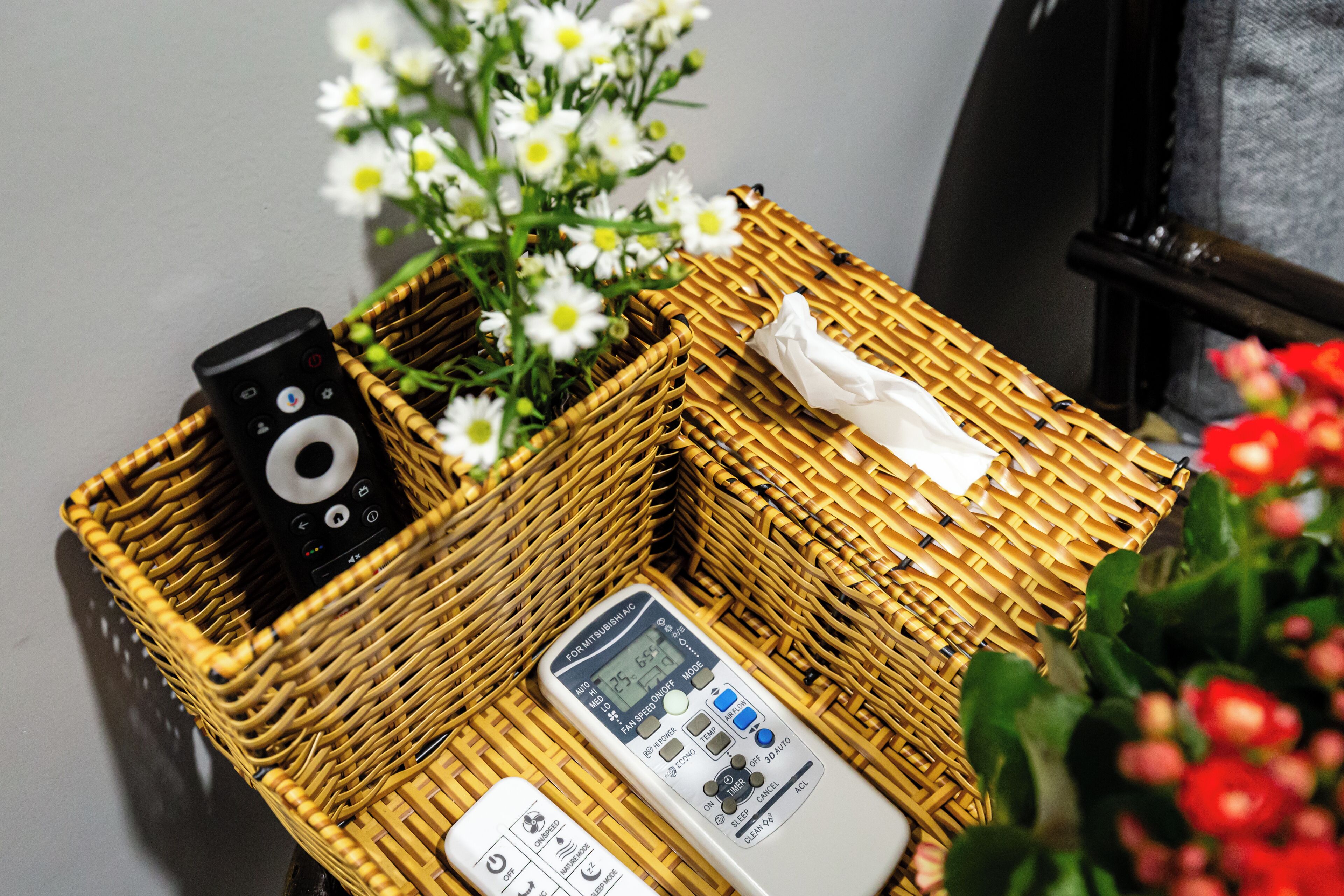 A wicker basket containing a remote control, a white device, and a tissue.