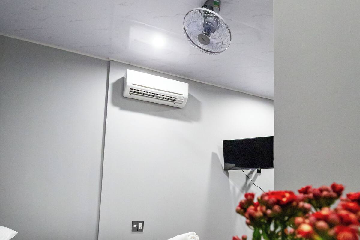 Een hotelkamer met een bed, een airconditioning, een plafondventilator en een televisie aan de muur.