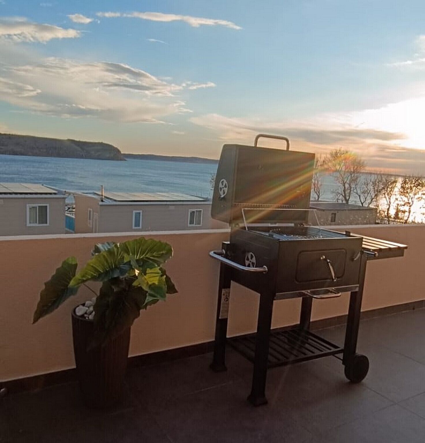Een barbecue op een balkon met uitzicht op zee en een verre kustlijn.