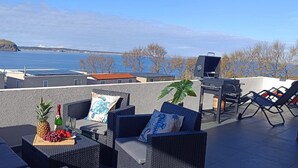 Eine Dachterrasse mit Gartenmöbeln, einem Grill und einem schönen Blick auf das Wasser.