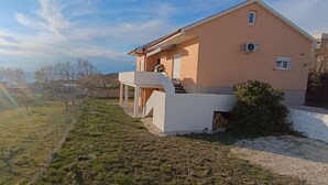 Ein zweistöckiges Haus mit Balkon, einem kleinen Garten und Blick auf ein Gewässer.