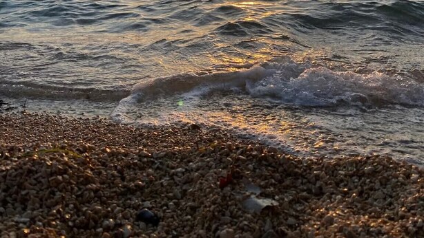 Ein Strand mit Kieselsteinen und Wellen bei Sonnenuntergang.