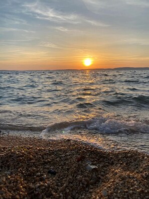 En strand med sten og bølger ved solnedgang.