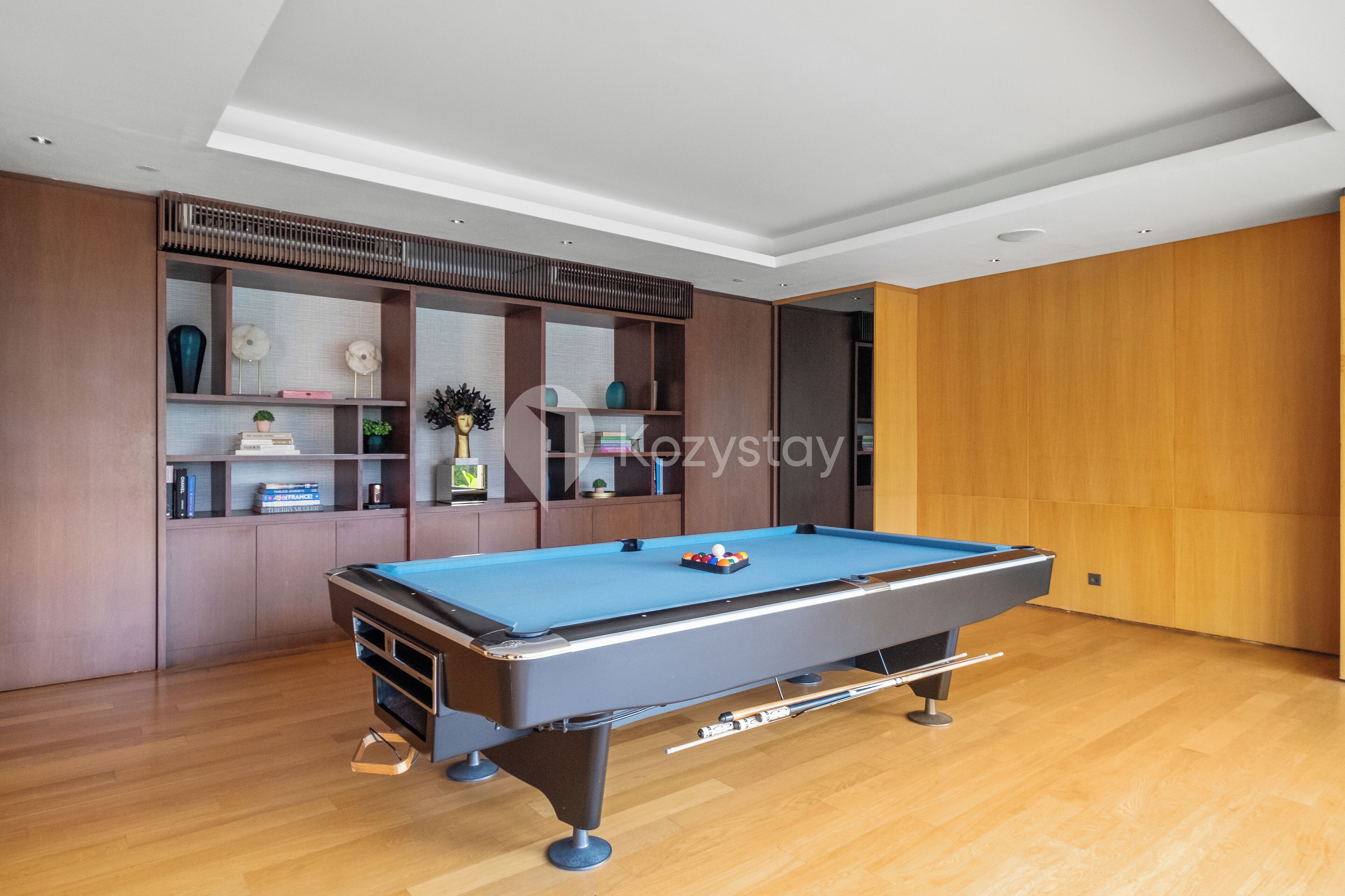A modern room with a pool table, wooden shelving with decorative items, and a wooden wall.