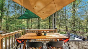 Eine Holzdiele mit Tisch und Stühlen, umgeben von einem Wald.