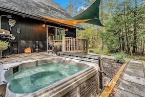 Ein Whirlpool vor einem Holzhaus mit einer Terrasse und einer überdachten Veranda.
