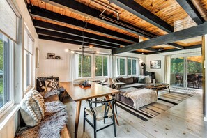 Un vaste espace de vie doté d’un plafond en bois, de grandes fenêtres, d’un coin salon confortable et d’une table à manger.