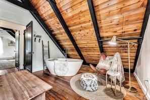 A modern bathroom with a freestanding bathtub, a wooden ceiling, and a towel rack.