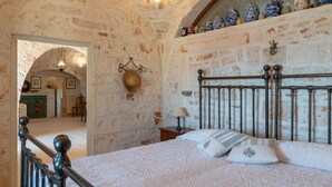 A bedroom with a stone wall, a bed with white bedding, and a nightstand with a lamp.