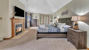 A bedroom with a fireplace, a bed, a nightstand, a TV, and a ceiling fan.