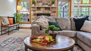 A cozy living room with a stone fireplace, a sectional sofa, a coffee table with a fruit platter, and a bench with cushions.